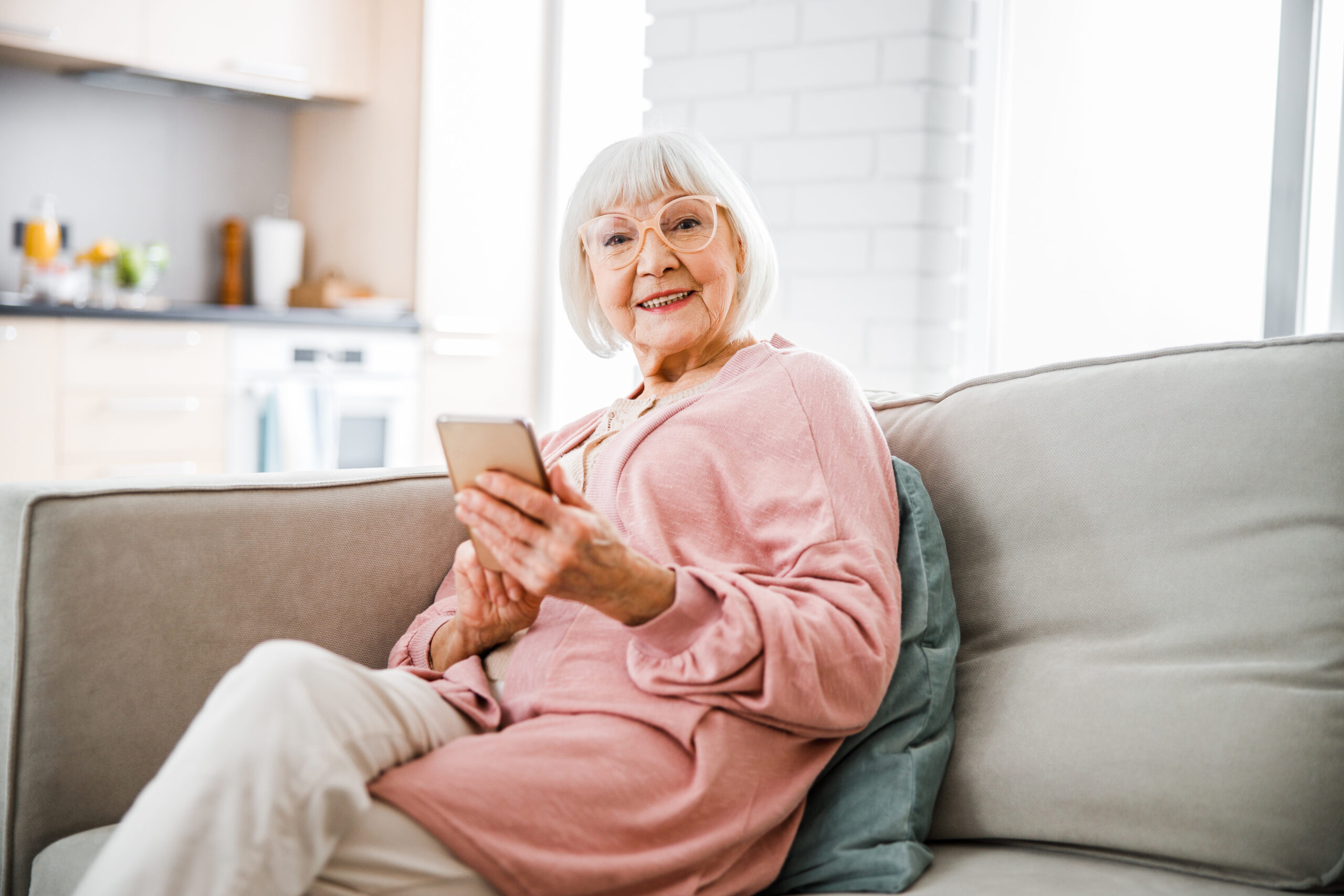 Smiling old lady sitting on couch and holding smartphone